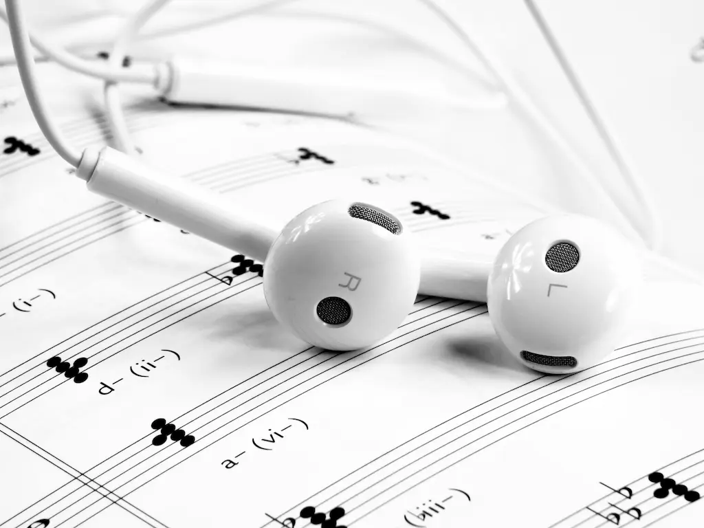 Weiße In-Ear-Kopfhörer liegen auf einem Notenblatt mit musikalischer Notation.